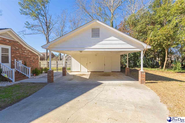 view of parking / parking lot with a carport, concrete driveway, and fence