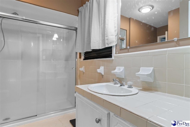 full bath with a stall shower, tile walls, vanity, and a textured ceiling