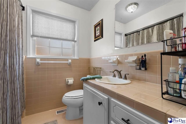 bathroom featuring toilet, a wainscoted wall, visible vents, vanity, and tile walls