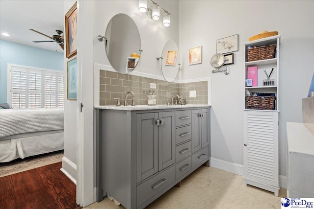 ensuite bathroom featuring double vanity, decorative backsplash, ensuite bathroom, ceiling fan, and baseboards