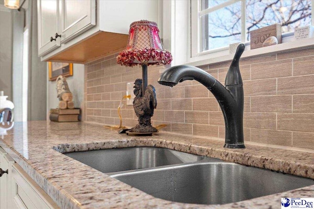 details featuring decorative backsplash, a sink, white cabinetry, and light stone countertops