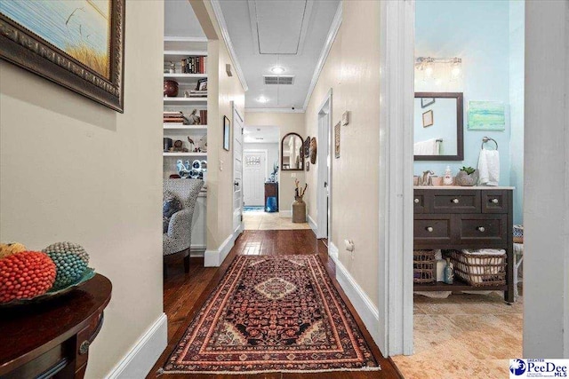 hall featuring wood finished floors, visible vents, baseboards, attic access, and crown molding