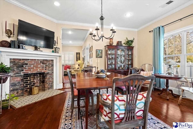 dining area featuring ornamental molding, a brick fireplace, visible vents, and wood finished floors