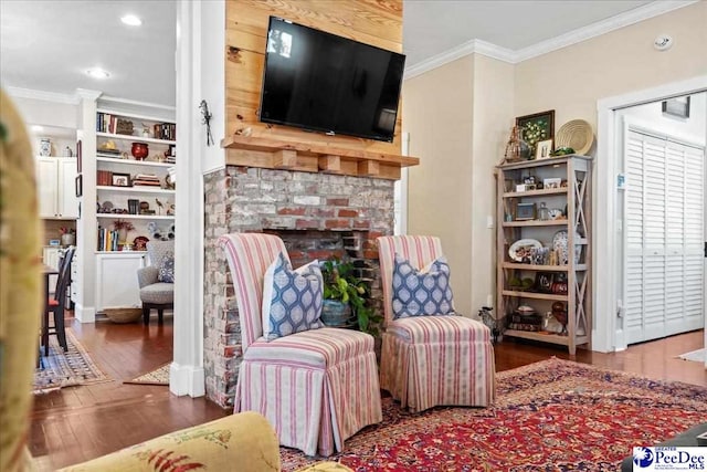 living area with a brick fireplace, ornamental molding, and wood finished floors