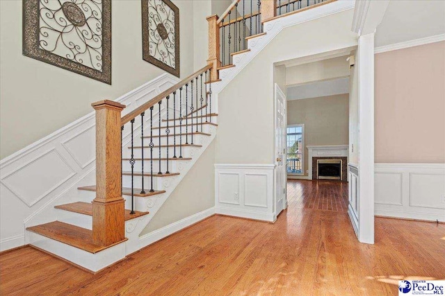 staircase with wood-type flooring, a towering ceiling, and ornamental molding