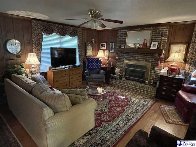 living room with hardwood / wood-style floors, wooden walls, a brick fireplace, and ceiling fan