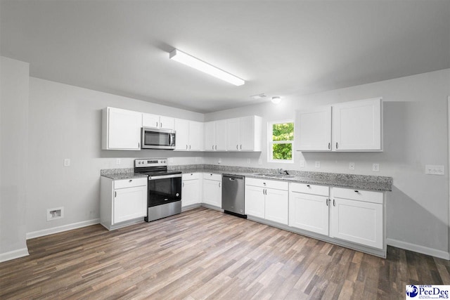 kitchen featuring baseboards, light wood-style floors, white cabinetry, a sink, and appliances with stainless steel finishes