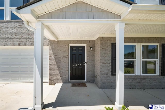doorway to property with brick siding, an attached garage, and covered porch