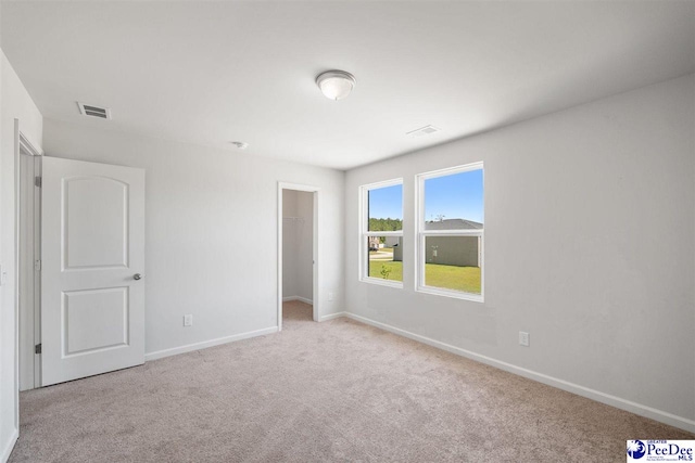 unfurnished bedroom with baseboards, visible vents, a walk in closet, and carpet