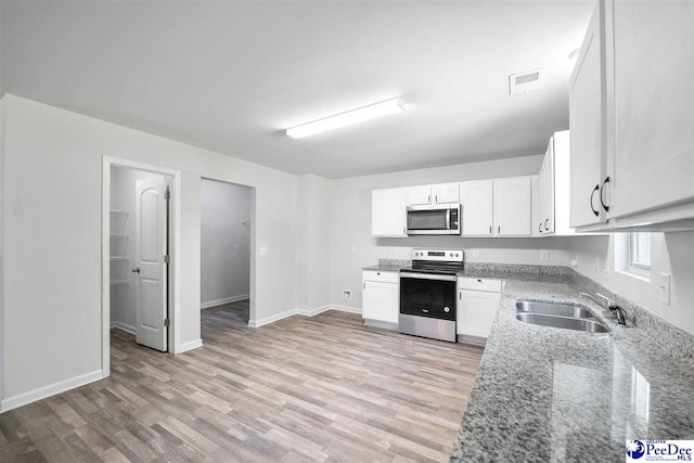 kitchen with a sink, light stone countertops, stainless steel appliances, and light wood-style flooring