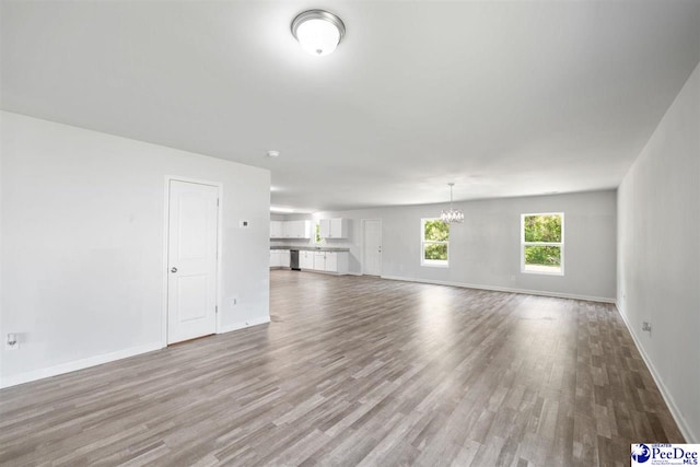 unfurnished living room with baseboards, wood finished floors, and a notable chandelier