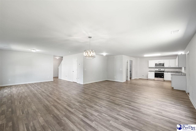 unfurnished living room with baseboards, wood finished floors, and a notable chandelier