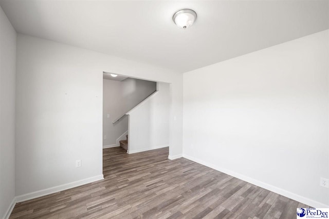 empty room with baseboards, stairs, and wood finished floors