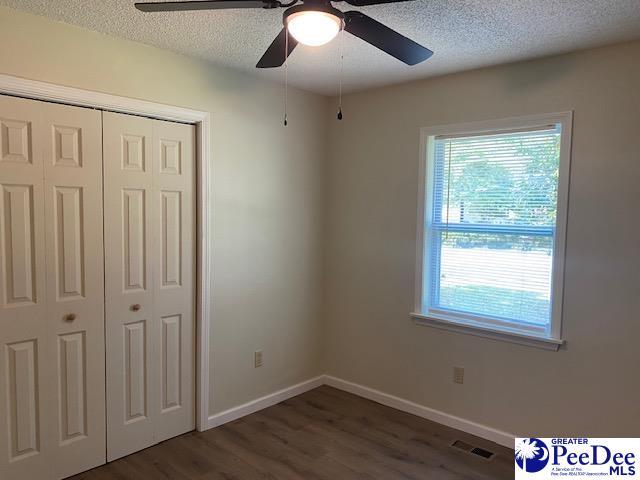 unfurnished bedroom with dark hardwood / wood-style flooring, ceiling fan, a closet, and a textured ceiling