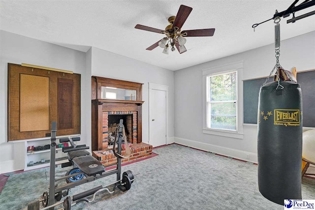 workout area with ceiling fan, a brick fireplace, carpet floors, and a textured ceiling