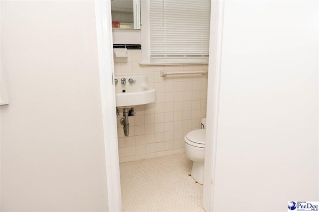 bathroom with toilet, sink, and tile walls