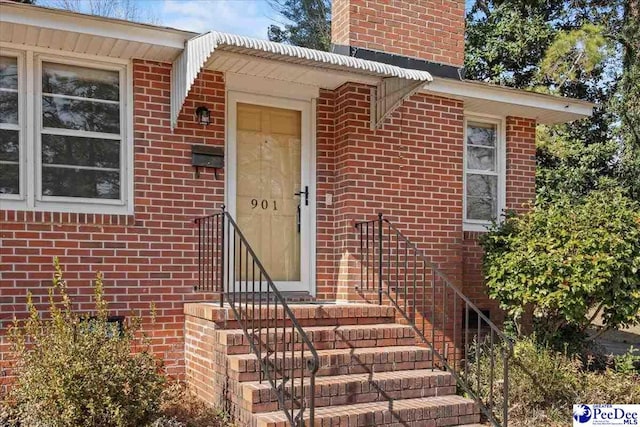 view of exterior entry featuring brick siding and a chimney