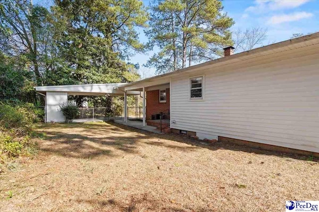 back of house featuring an attached carport, a lawn, and fence