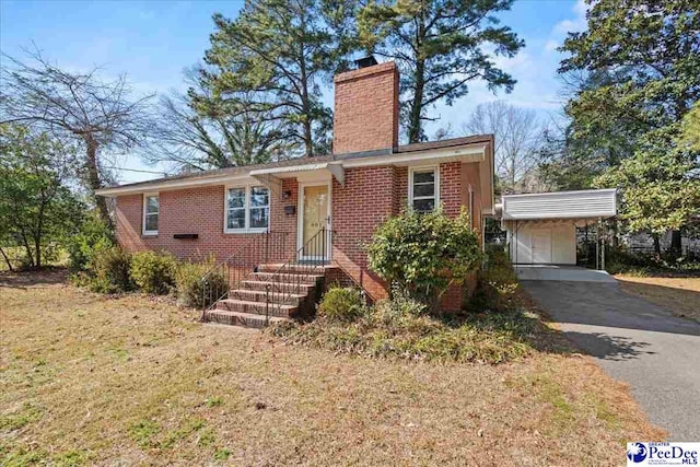 view of front facade featuring brick siding, driveway, a carport, a chimney, and a front yard