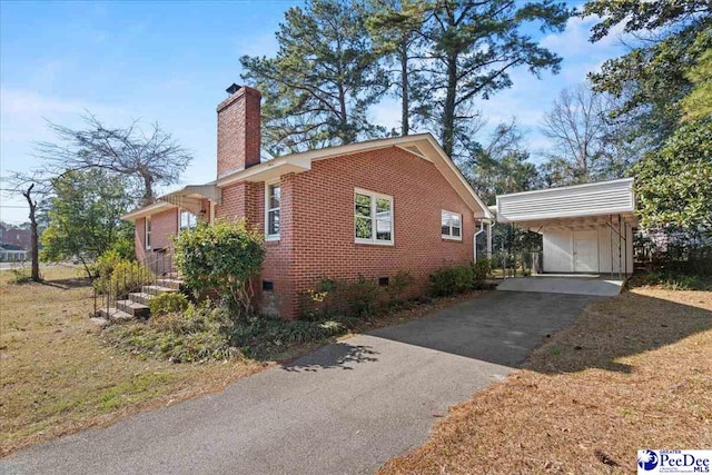 view of side of property featuring aphalt driveway, an outbuilding, brick siding, a chimney, and crawl space