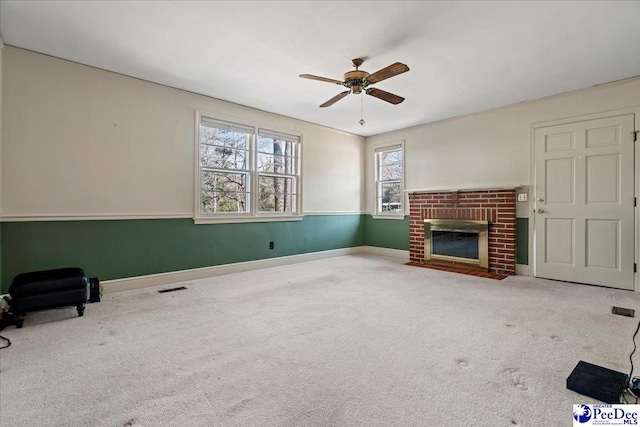 unfurnished living room with carpet floors, visible vents, a ceiling fan, a brick fireplace, and wainscoting