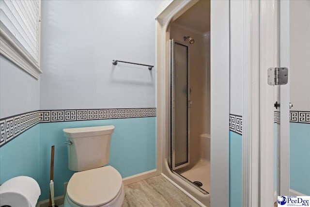 bathroom featuring baseboards, wood finished floors, toilet, and a shower stall