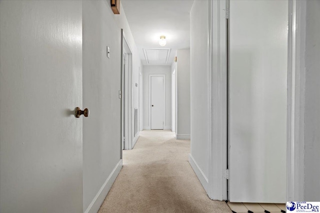 hall with attic access, light colored carpet, and baseboards