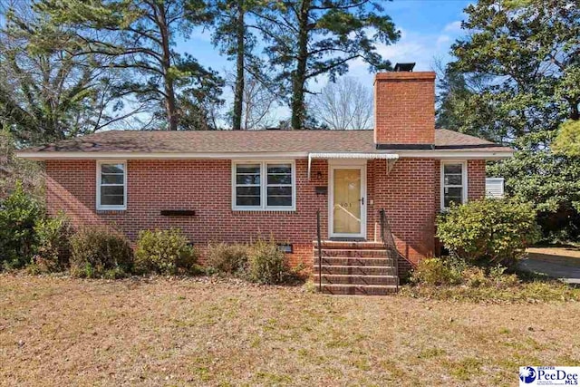 view of front of property featuring entry steps, brick siding, a chimney, and a front lawn