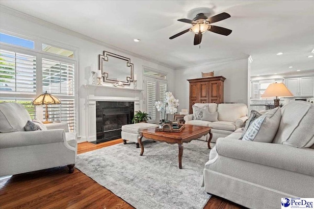 living area featuring ceiling fan, recessed lighting, a fireplace with flush hearth, dark wood-type flooring, and ornamental molding