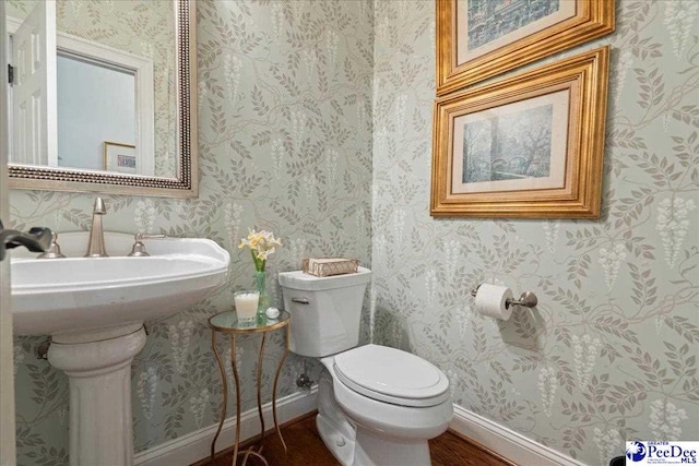 bathroom with toilet, wallpapered walls, and baseboards