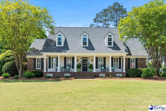 cape cod house featuring a porch, brick siding, a front yard, and roof with shingles