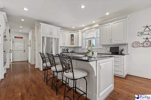 kitchen with decorative backsplash, a kitchen bar, dark wood-style flooring, dark countertops, and high end refrigerator