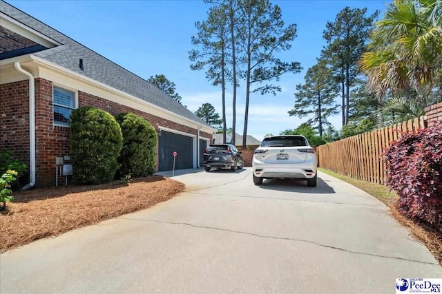 view of property exterior featuring fence, brick siding, a shingled roof, an attached garage, and driveway