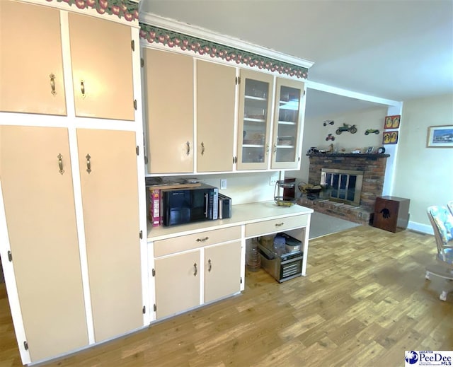 kitchen featuring crown molding, a brick fireplace, white cabinets, and light hardwood / wood-style floors