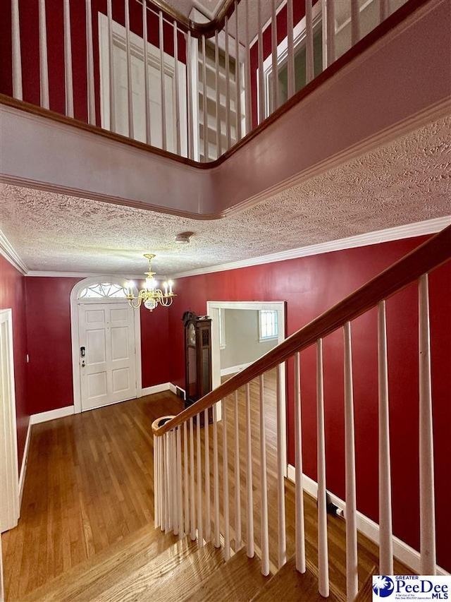 entrance foyer with crown molding, hardwood / wood-style flooring, a towering ceiling, a textured ceiling, and a chandelier