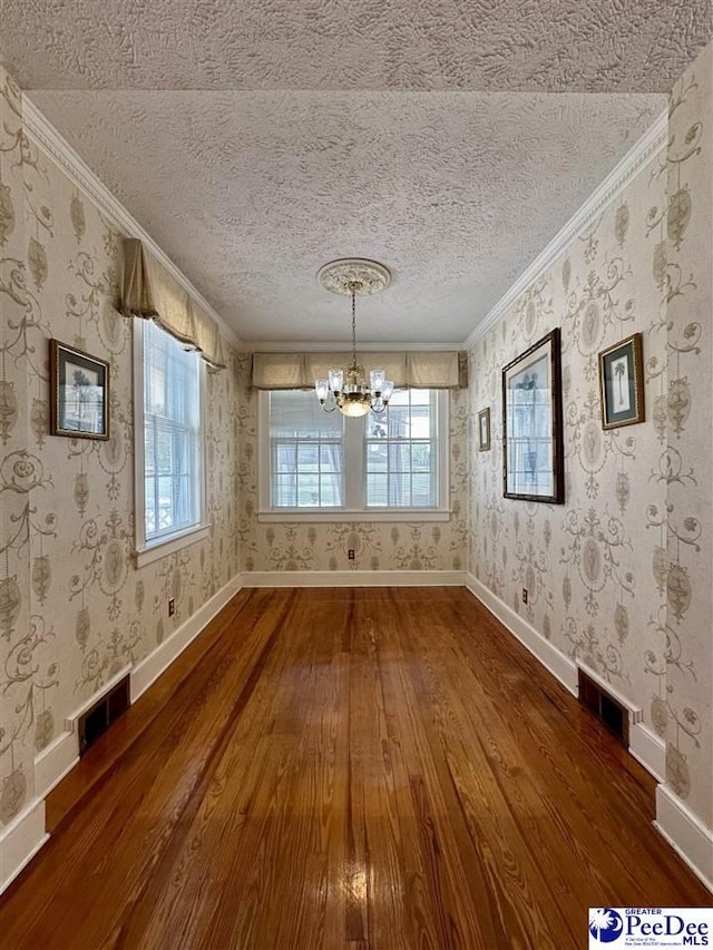 unfurnished dining area featuring hardwood / wood-style floors, a chandelier, crown molding, a healthy amount of sunlight, and a textured ceiling