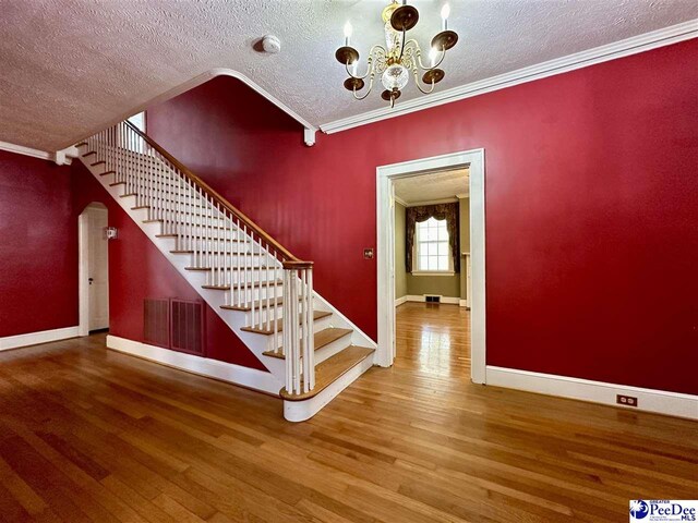 stairs with hardwood / wood-style flooring, ornamental molding, a chandelier, and a textured ceiling