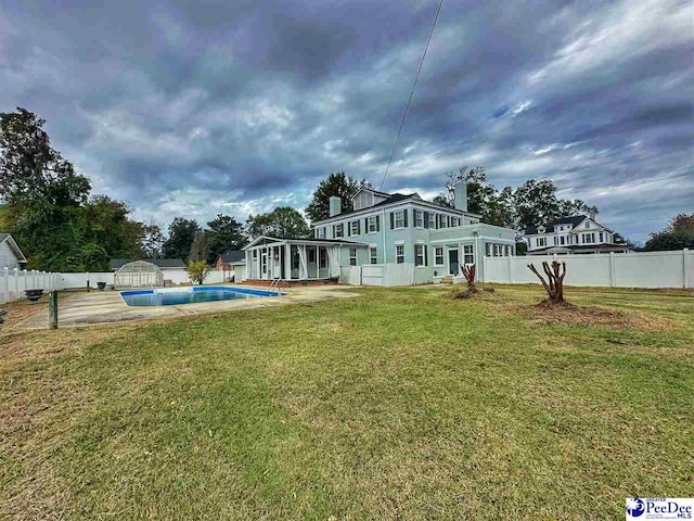 rear view of property featuring a fenced in pool, a sunroom, a storage unit, and a lawn