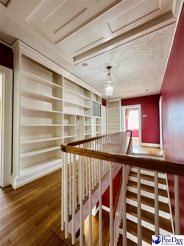 corridor featuring wood-type flooring, a textured ceiling, and a notable chandelier