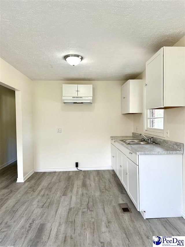 kitchen featuring sink, a textured ceiling, white cabinets, and light wood-type flooring