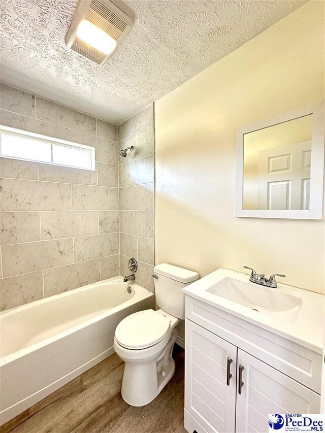 full bathroom featuring toilet, wood-type flooring, a textured ceiling, vanity, and tiled shower / bath combo