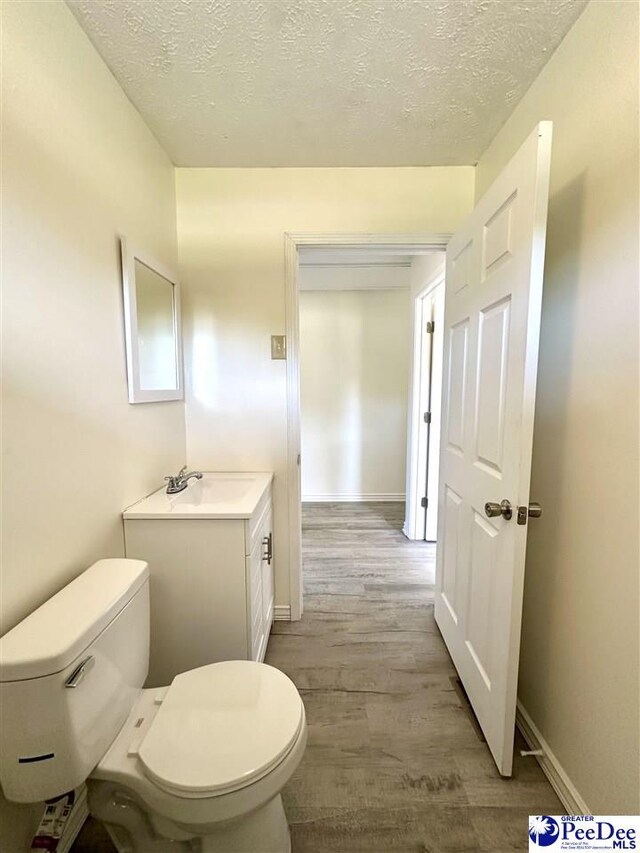 bathroom with wood-type flooring, toilet, vanity, and a textured ceiling