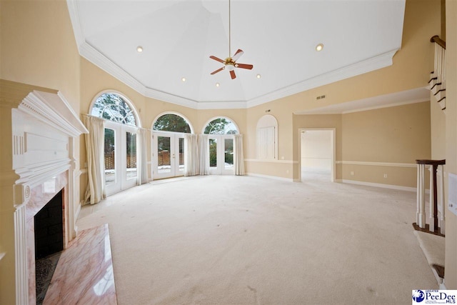 unfurnished living room with crown molding, a premium fireplace, ceiling fan, a high ceiling, and light carpet