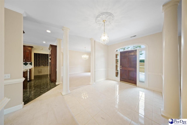 tiled entryway featuring decorative columns, ornamental molding, and a notable chandelier