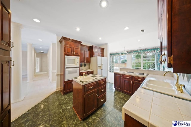 kitchen featuring sink, white appliances, decorative columns, and a kitchen island