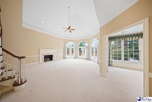 unfurnished living room with high vaulted ceiling, crown molding, ceiling fan, a premium fireplace, and light carpet