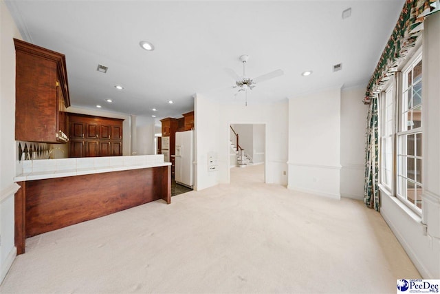 kitchen with crown molding, light carpet, tile counters, kitchen peninsula, and white fridge with ice dispenser