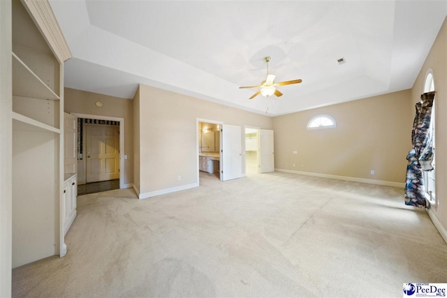 unfurnished bedroom with light carpet, ensuite bath, and a raised ceiling