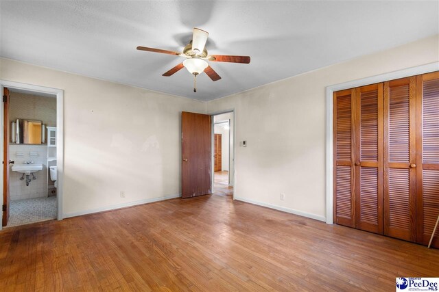unfurnished bedroom with a closet, a ceiling fan, wood finished floors, baseboards, and a sink