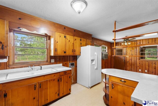 kitchen with brown cabinets, a sink, white refrigerator with ice dispenser, light countertops, and wood walls